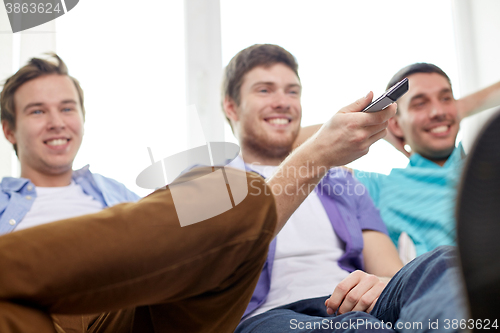 Image of happy male friends with remote watching tv at home
