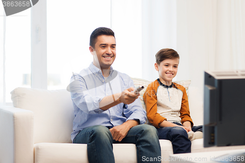 Image of smiling father and son watching tv at home