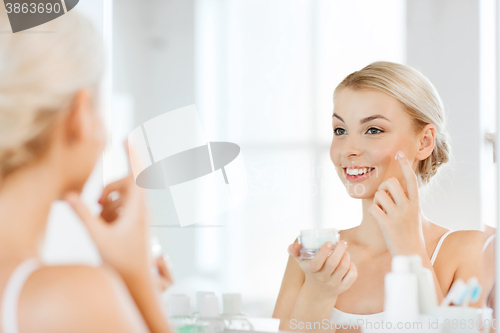 Image of happy woman applying cream to face at bathroom