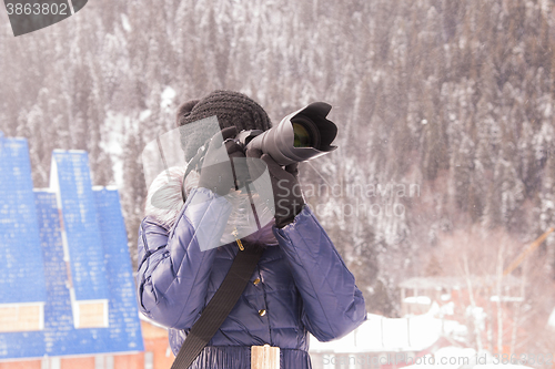 Image of A young girl takes pictures winter mountain landscape in a snow storm on a SLR camera with telephoto lens