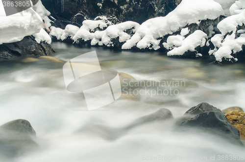 Image of Mountain river flowing between the rock and snow-covered branches of trees, photographed with a long exposure