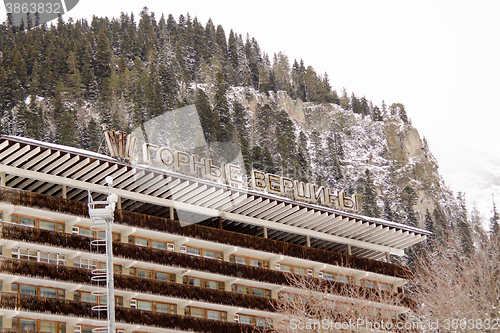 Image of Dombay, Russia - February 7, 2015: The top part of the facade of the hotel \"Mountain peaks\" on a background of snow-capped mountains, located in the small town of Dombay Street. Karachai, 117