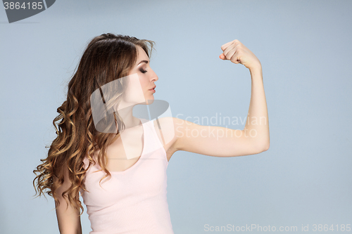 Image of The young woman showing her muscles on gray background. 