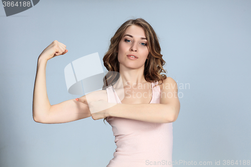 Image of The young woman showing her muscles on gray background. 