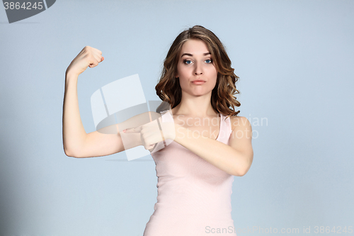 Image of The young woman showing her muscles on gray background. 