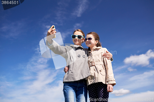 Image of happy girls with smartphone taking selfie outdoors