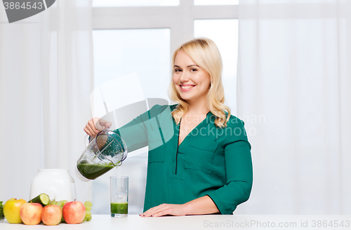 Image of happy woman with blender jug pouring juice at home