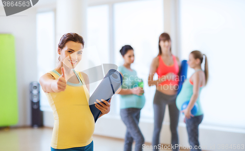 Image of pregnant woman with mat in gym showing thumbs up 