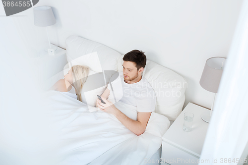 Image of man texting message while woman is sleeping in bed