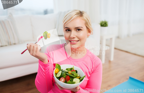 Image of smiling young woman eating salad at home