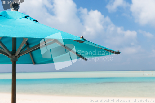 Image of parasol over blue sky and beach