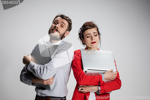 Image of The young businessman and businesswoman with laptops  posing on gray background