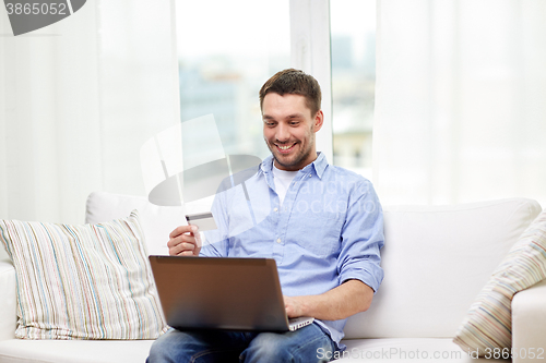 Image of smiling man with laptop and credit card at home