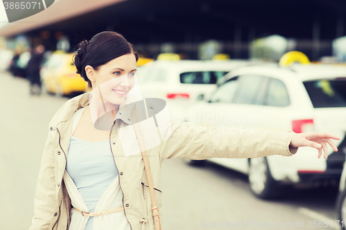 Image of smiling young woman waving hand and catching taxi