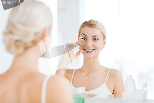 Image of woman with curler curling eyelashes at bathroom