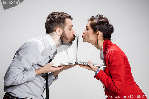 Image of The young businessman and businesswoman with laptops kissing screens on gray background
