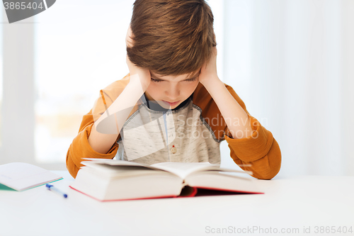 Image of student boy reading book or textbook at home