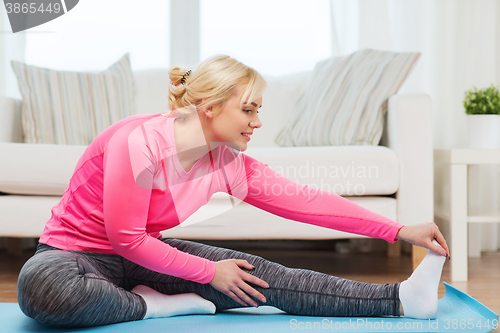 Image of happy woman stretching leg on mat at home