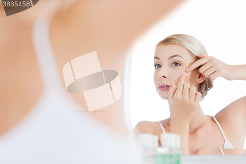 Image of woman squeezing pimple at bathroom mirror