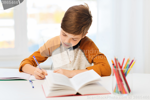 Image of student boy with book writing to notebook at home