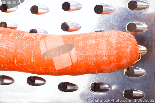 Image of grated carrots. Nearby is grater and carrots