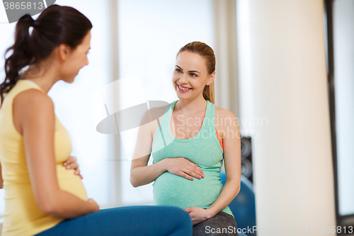 Image of two happy pregnant women sitting on balls in gym