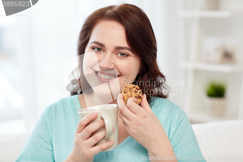 Image of happy plus size woman with cup and cookie at home