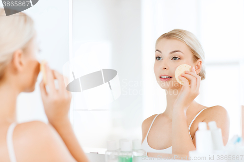 Image of young woman washing face with sponge at bathroom