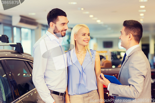 Image of happy couple with car dealer in auto show or salon