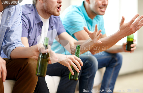 Image of happy male friends with beer watching tv at home