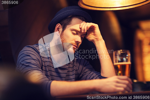 Image of unhappy lonely man drinking beer at bar or pub