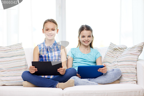 Image of happy girls with tablet pc sitting on sofa at home