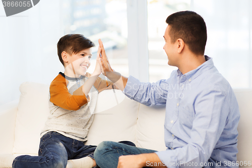 Image of happy father and son doing high five at home