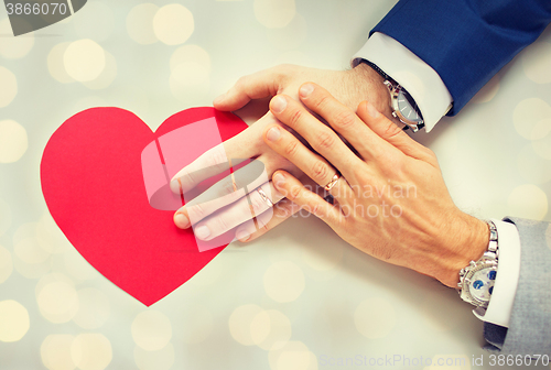 Image of close up of male gay couple hands with red heart