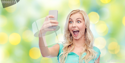 Image of smiling young woman taking selfie with smartphone