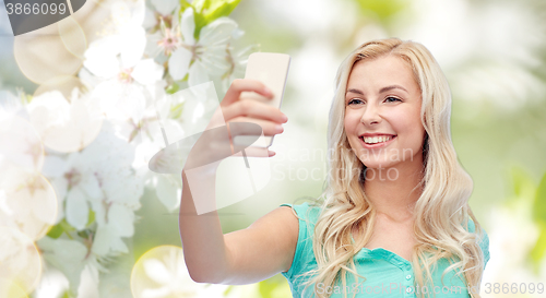 Image of smiling young woman taking selfie with smartphone