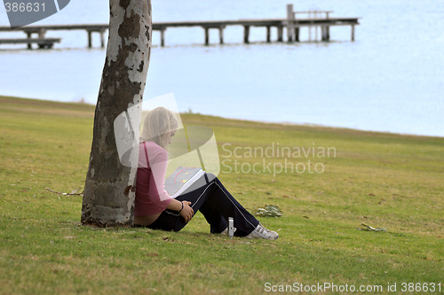 Image of girl sitting against tree reading book