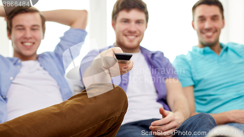 Image of happy male friends with remote watching tv at home