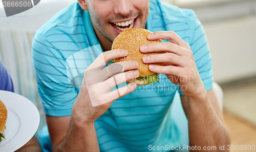 Image of close up of happy man eating hamburger at home