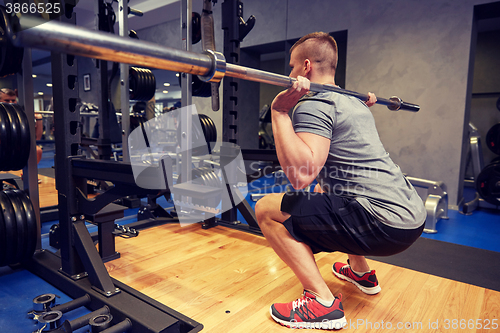 Image of young man flexing muscles with bar in gym