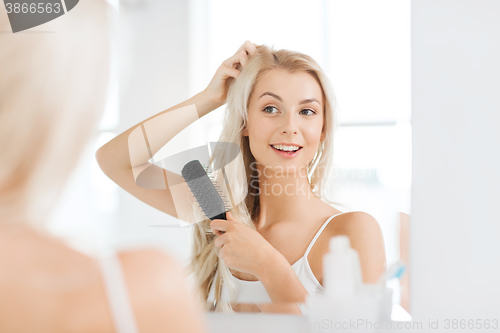 Image of happy woman brushing hair with comb at bathroom