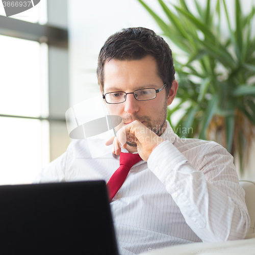 Image of Businessman in office reading on laptop computer.