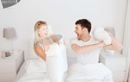 Image of happy couple having pillow fight in bed at home