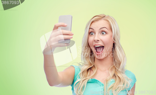 Image of smiling young woman taking selfie with smartphone