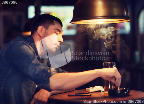 Image of man drinking beer and smoking cigarette at bar