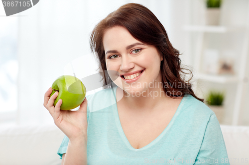 Image of happy plus size woman eating green apple at home