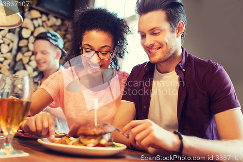 Image of happy friends eating and drinking at bar or pub