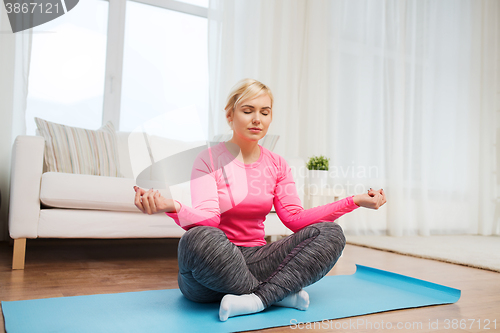 Image of happy woman stretching leg on mat at home