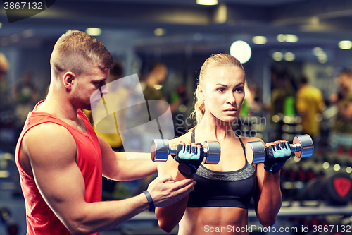 Image of young couple with dumbbells flexing muscles in gym