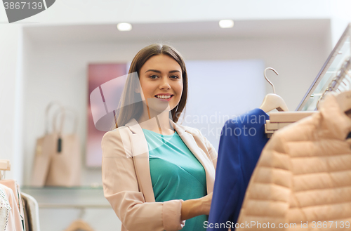 Image of happy young woman choosing clothes in mall